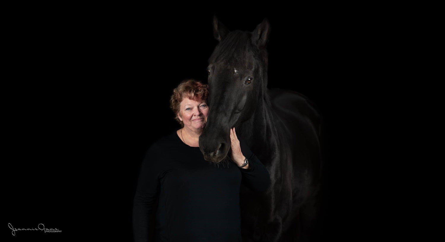 Woman standing next to a black horse against a dark background